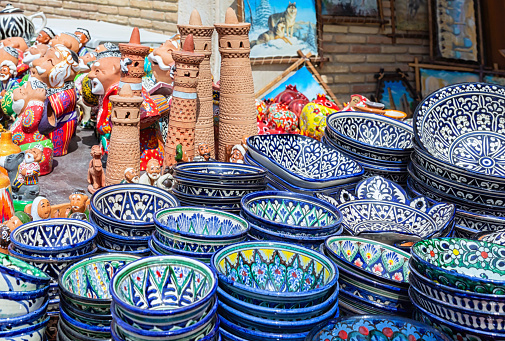 Ornamented ceramic bowls and models of Islam-Khodja (Islomxo'ja) minaret. Typical handmade Khiva's souvenires. Close-up, selected focus. Khiva (Xiva), Uzbekistan. April 10, 2023