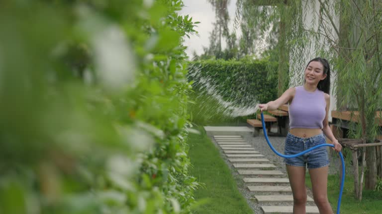 Active young woman watering hedge in garden with hose, summer gardening activities