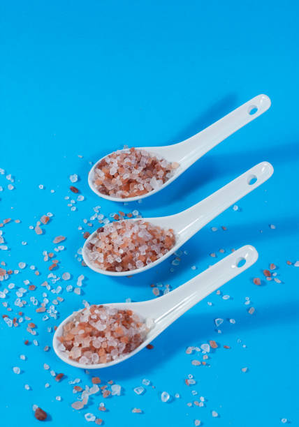istock Composition of ceramic teaspoons with Himalayan pink salt on blue background. 2136420899