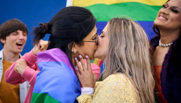 junges kaukasisches lesbisches paar küsst sich liebevoll mit regenbogenfahnen und feiert mit lgbt - sex symbol couple kissing women stock-fotos und bilder