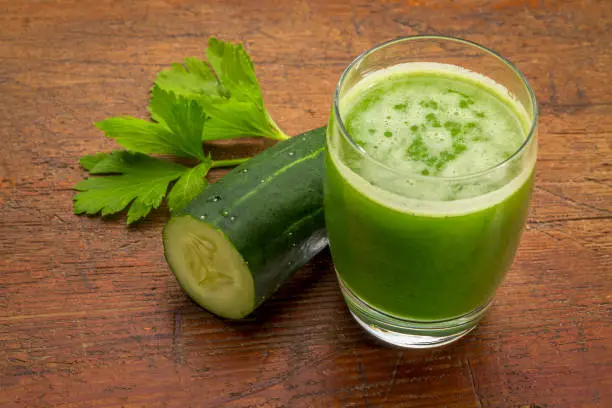 glass of fresh green vegetable juice with cucumber and celery leaf against grunge wood