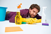 A man lies on the floor with a bucket of detergents providing services light background