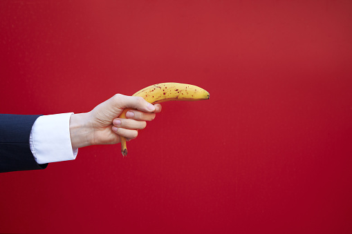 Hand of a manager holding a banana as if shooting from a gun, with copy space