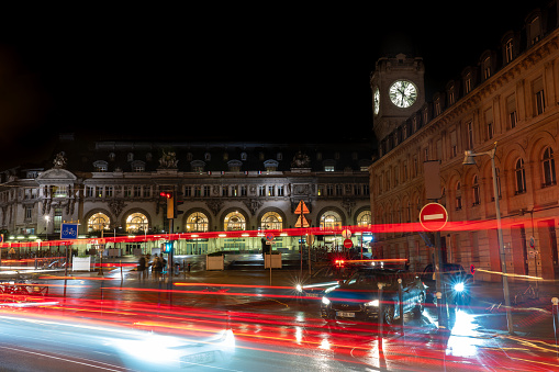 Low exposure photograph of passing vehicle lights and cars waiting for the traffic light to change in front of the Gare de Lyon facade. Paris. France. August 11, 2023.