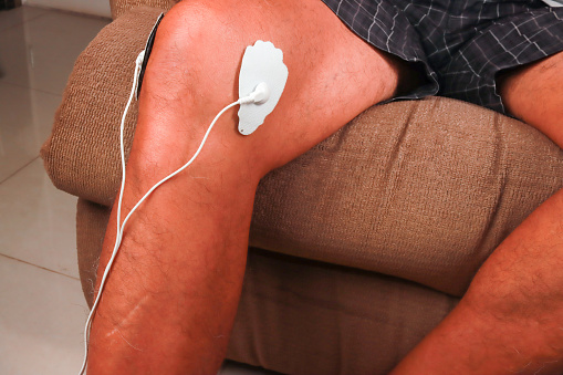Man using an Electro Therapy Massager or Tens Unit on his knee for pain relief of Muscles and Joint