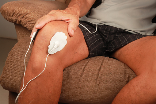 Man using an Electro Therapy Massager or Tens Unit on his knee for pain relief of Muscles and Joint