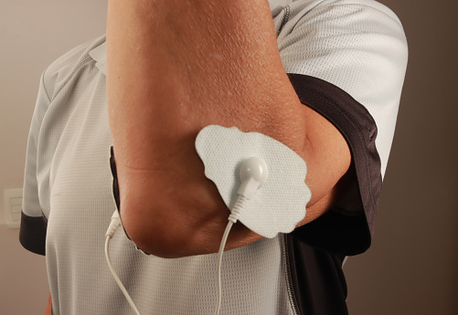 Man using an Electro Therapy Massager or Tens Unit on his elbow for pain relief of Muscles and Joint