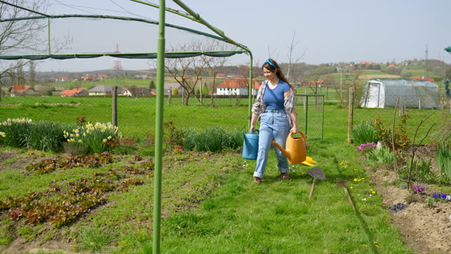 SLO MO Happy Young Woman Gardener Walking with Watering Cans in Garden on Sunny Day