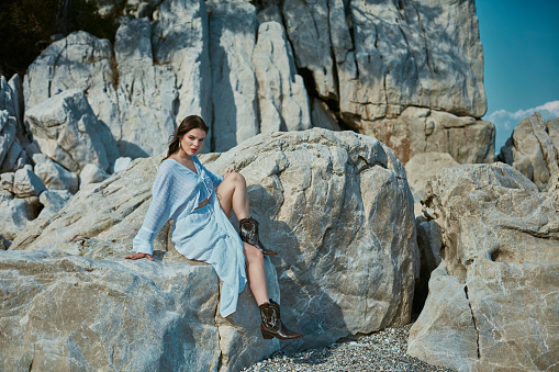Beautiful woman sitting on the rocks on the beach, enjoying the beautiful weather, sunbathing.