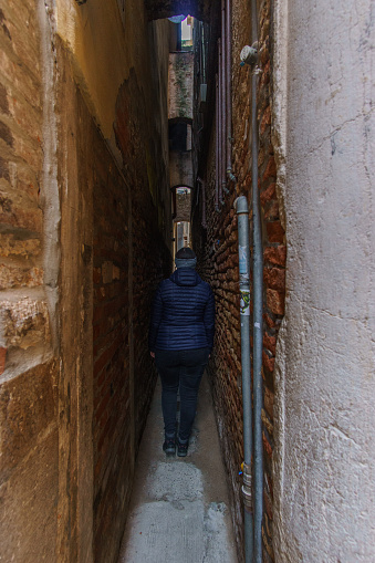 Tourist standing in the most narrow alley Calle Varisco in Venice, Veneto, Italy