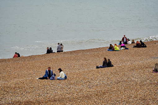 Brighton, Brighton And Hove City, East Sussex, Southeastern England, United Kingdom, Britain, Europe - 16th March 2024: several people on the beach.

Many local English people are sitting on Brighton Beach on a cloudy and sunny midday in spring, with the sparkling moody sea serving as the breathtaking backdrop in the photo, showcasing the stunning English Channel coastline that connects to the vastness of the Atlantic Ocean.