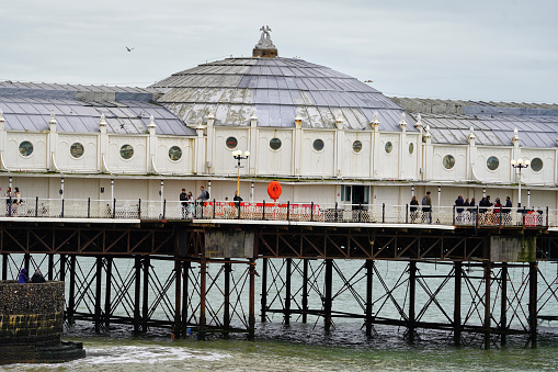 Brighton, Brighton And Hove, East Sussex, Southeastern England, United Kingdom, Britain, Europe - 16th March 2024: Brighton Seafront. The Brighton palace pier structure and facade near the Brighton beach. Some people are also seen from the distance walking on the structure.\n\nLocation: Brighton Palace Pier is located at Madeira Drive, Brighton, BN2 1TW, in the city centre opposite the Old Steine.\n\nIts Structure and Attractions as seen in the photo:\nBrighton Palace Pier, a Grade II listed pleasure pier building, features a variety of attractions including traditional British architecture, modern entertainment facilities, fairground rides, roller coasters, restaurants, arcades, and some Restaurants. a waterfront theme park in England.\n\nThe seafront of Brighton and Hove in England;  a picturesque view of the beach, a sought-after travel destination in the UK. A vibrant atmosphere and charming coastal town appeal, Brighton and Hove's  panoramic view that captivates tourists from all over.