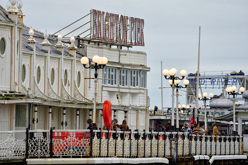 Brighton, Brighton And Hove, East Sussex, Southeastern England, United Kingdom, Britain, Europe - 16th March 2024: Brighton Seafront. The Brighton palace pier structure and facade near the Brighton beach. Some people are also seen from the distance walking on the structure.

Location: Brighton Palace Pier is located at Madeira Drive, Brighton, BN2 1TW, in the city centre opposite the Old Steine.

Its Structure and Attractions as seen in the photo:
Brighton Palace Pier, a Grade II listed pleasure pier building, features a variety of attractions including traditional British architecture, modern entertainment facilities, fairground rides, roller coasters, restaurants, arcades, and some Restaurants. a waterfront theme park in England.

The seafront of Brighton and Hove in England;  a picturesque view of the beach, a sought-after travel destination in the UK. A vibrant atmosphere and charming coastal town appeal, Brighton and Hove's  panoramic view that captivates tourists from all over.