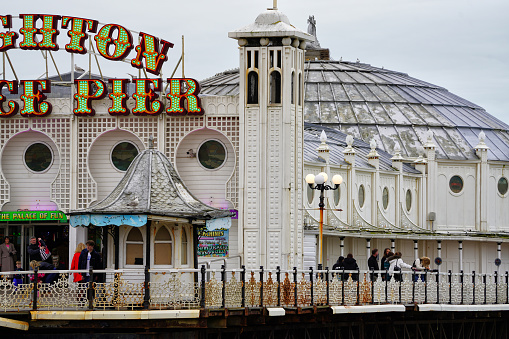 Brighton, Brighton And Hove, East Sussex, Southeastern England, United Kingdom, Britain, Europe - 16th March 2024: Brighton Seafront. The Brighton palace pier structure and facade near the Brighton beach. Some people are also seen from the distance walking on the structure.

Location: Brighton Palace Pier is located at Madeira Drive, Brighton, BN2 1TW, in the city centre opposite the Old Steine.

Its Structure and Attractions as seen in the photo:
Brighton Palace Pier, a Grade II listed pleasure pier building, features a variety of attractions including traditional British architecture, modern entertainment facilities, fairground rides, roller coasters, restaurants, arcades, and some Restaurants. a waterfront theme park in England.

The seafront of Brighton and Hove in England;  a picturesque view of the beach, a sought-after travel destination in the UK. A vibrant atmosphere and charming coastal town appeal, Brighton and Hove's  panoramic view that captivates tourists from all over.