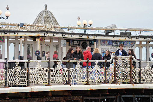 Brighton, Brighton And Hove, East Sussex, Southeastern England, United Kingdom, Britain, Europe - 16th March 2024:\n\nA Vibrant Scene: Locals and Tourists Stroll Along Iconic Brighton Seafront in the Coastal Fishing Town of Brighton. The Promenade on the Brighton palace pier, adorned with Blue Railings, Bustles with Activity on Brighton Beach. Embracing the English City of Brighton and Hove in East Sussex, England, this Captivating View Belongs to the United Kingdom, Britain, and Europe on a Beautiful Spring Daytime.