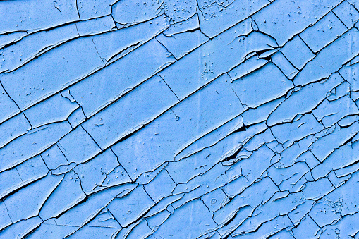 Old, weather- and time-damaged, peeling, cracked blue paint on the wall.