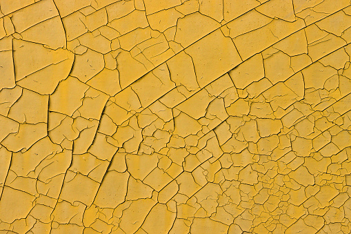 The texture of old, cracked, peeling, yellow-orange paint on metal.
