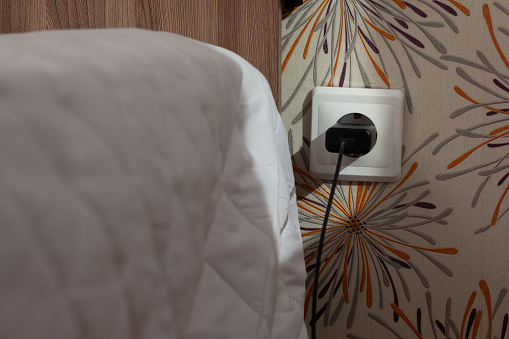Wall socket with charger plug inside close to bed on paper wall