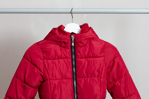 Red child puffer coat hanging over white background