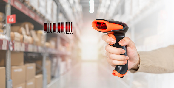A person is holding a barcode scanner in a warehouse. A person is holding a barcode scanner and the barcode is red. Concept of scanning a barcode and the mood is focused and determined