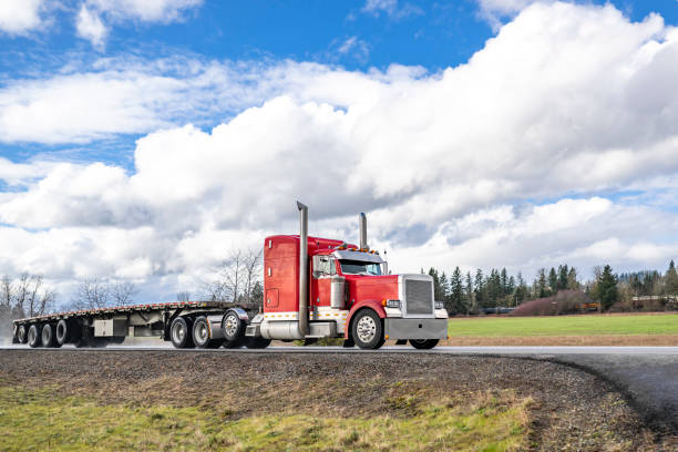 istock Powerful classic red big rig semi truck tractor with chrome parts transporting empty flat bed semi trailer driving on the wet after the rain narrow road 2136898908