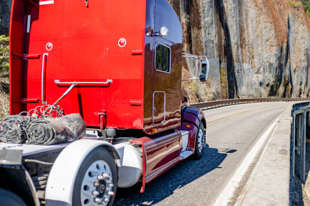 istock Red classic big rig semi truck tractor with high cab transporting flat bed semi trailer running on the mountain road around rock cliff wall 2136899422