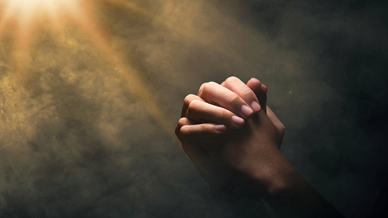 Christian man praying with raised hands on a bright light background. Christian concept