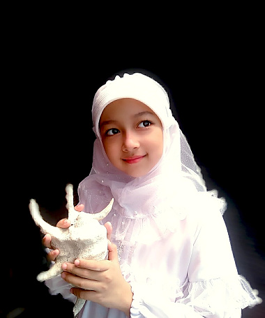 Indonesian hijab girl is holding a shell.
