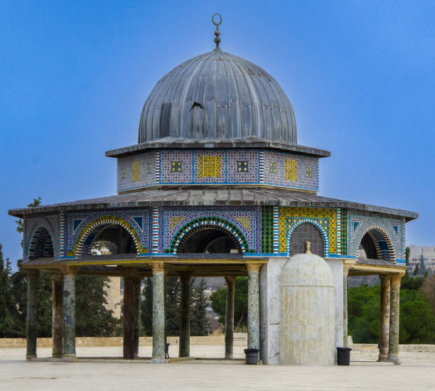 This image elegantly captures a gazebo, built by Ottomans, inside Al-Aqsa Mosque Complex, with a beautifully crafted domed roof, embellished with colorful mosaic tiles. Standing against the serene backdrop of a clear sky, the gazebo’s design reflects a blend of artistry and harmony with nature.