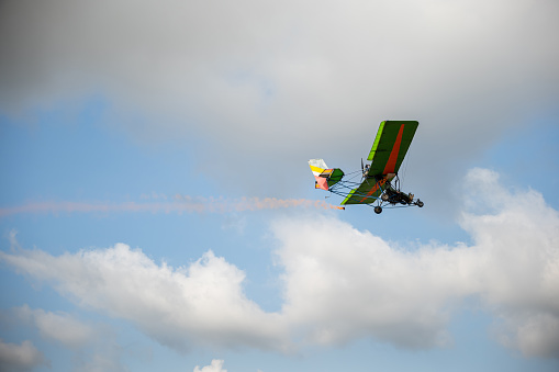 Stunt plane leaves smoke trail in aerobatic performance against blue sky. Skilled pilot maneuvers aeroplane showcasing acrobatic skills and aerial freedom.