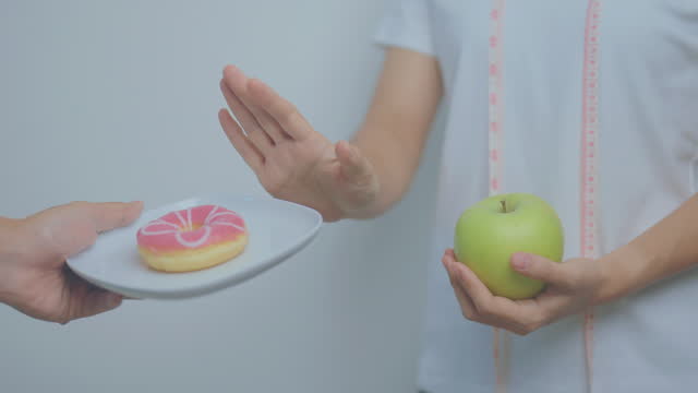 woman hand hold green Apple and reject donut, female fitness choose between fruit is Healthy and sweet is Unhealthy junk food. Dieting control, Weight loss, Obesity, eating lifestyle and nutrition