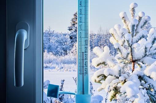 An outdoor thermometer is taped to outside of window glass and shows an air temperature of 20 degrees below zero Celsius.