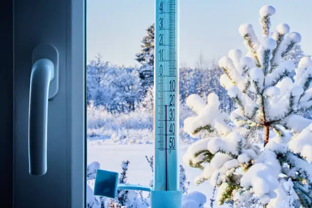 Photo of Air temperature is 20 degrees below zero Celsius on scale of an outdoor thermometer, fixed to window glass with adhesive tape on  outside.