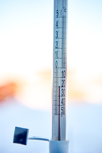 An outdoor thermometer is mounted on window glass using adhesive tape, scale shows 20 degrees Celsius below zero.