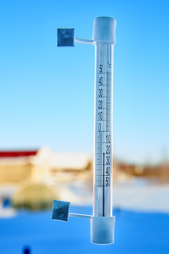 An outdoor thermometer is attached with adhesive tape to window glass outside, on scale of 20 degrees below zero Celsius.