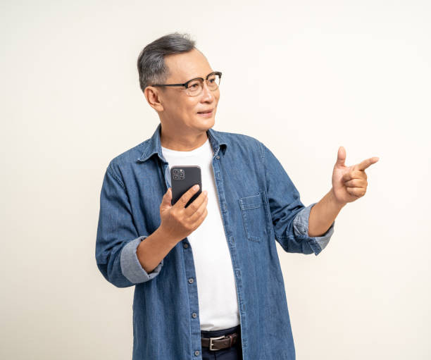istock Handsome asian mature old man using smartphone palm up  pointing hand on copy space isolated white background. Portrait of cheerful smiling senior asian man holding cell phone. Mature People and lifestyle 2137096117