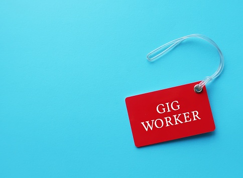 Red tag on blue copy space background with text GIG WORKER - someone who works in gig economy as independent contractor or freelancer, self-employed rather than employees