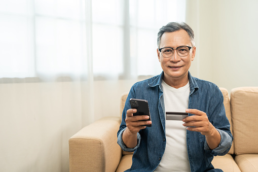 Mature asian old man holding credit card input number in smartphone for payment online. Pay with credit card on cell phone lifestyle technology financial for senior people