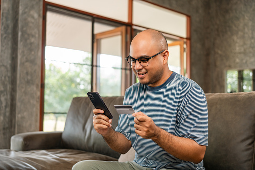 Asian handsome man holding credit card input number in smartphone for payment online. Pay with credit card on cell phone lifestyle technology financial for people