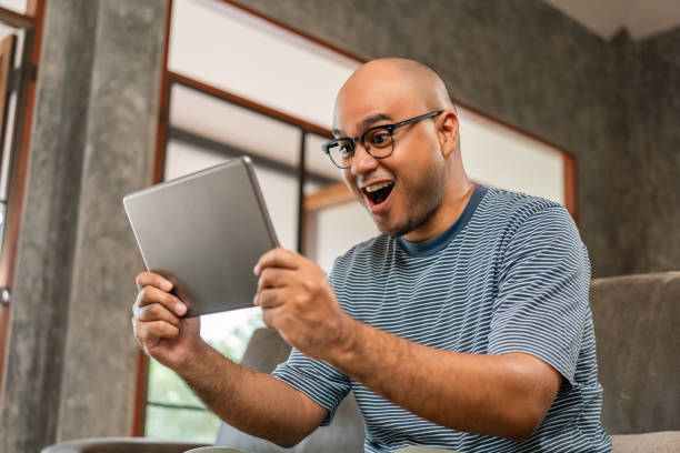 istock Young asian man sit and relax in the living room on the sofa. He using texting on tablet reading news today in the morning 2137112365