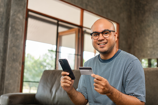 Asian handsome man holding credit card input number in smartphone for payment online. Pay with credit card on cell phone lifestyle technology financial for people