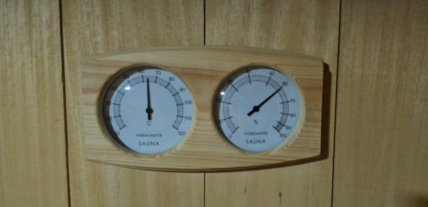 A cozy wooden sauna interior featuring a thermometer and hygrometer mounted on a shelf alongside a small brown bottle and a cloth, providing a warm and inviting atmosphere for relaxation.