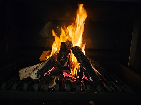 A fire burning fiercely in a fireplace, showing bright, vibrant flames flickering and dancing. The intense heat radiates from the flames, illuminating the space with a warm glow.