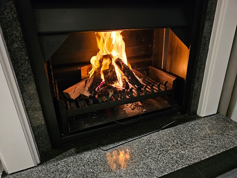 A fire is burning brightly in a fireplace within a cozy room, providing warmth and illumination. The flames flicker and dance, casting a warm glow around the space.