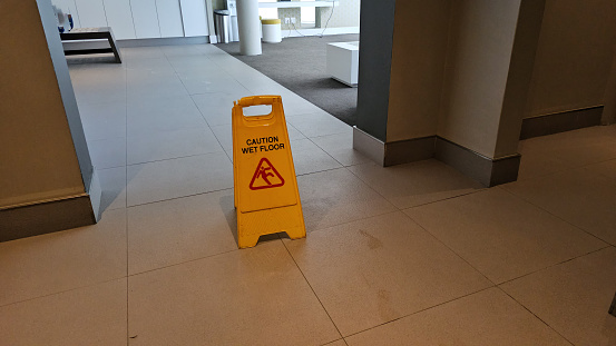 A yellow caution sign is placed on top of a tiled floor. The sign alerts individuals to proceed with care in the area.