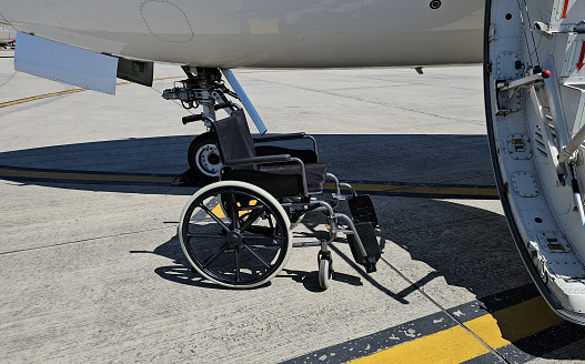 A wheelchair is securely attached to the side of an airplane, likely to assist passengers with disabilities boarding or disembarking the aircraft. The image shows the wheelchair safely suspended in place next to the planes entrance.