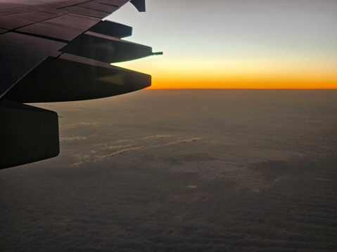 The wing of an airplane is silhouetted against the setting sun, showcasing the vibrant hues of the sky as daylight fades.