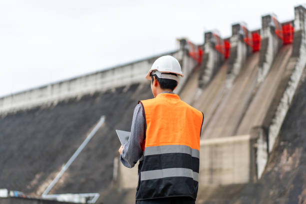 Professional asian maintenance engineer man with safety helmet in construction site dam with hydroelectric power plant and irrigation. Manager engineer man working with tablet at project big building.