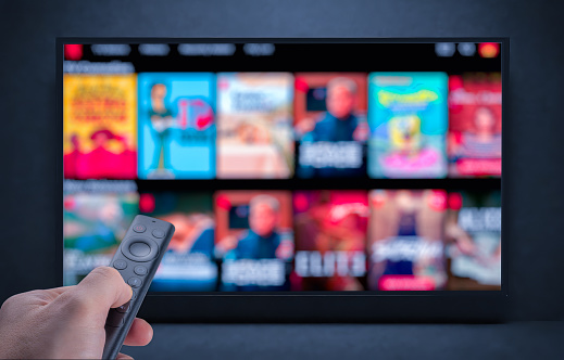 Multimedia streaming concept. Hand holding remote control. TV screen with lot of pictures. Television streaming. VoD content provider. Video service with internet streaming multimedia shows, series.
