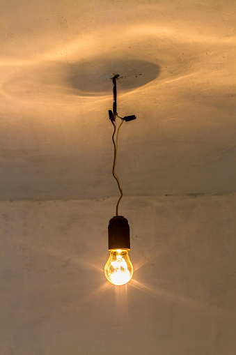 An old incandescent light bulb. A light bulb turned on in an old room.